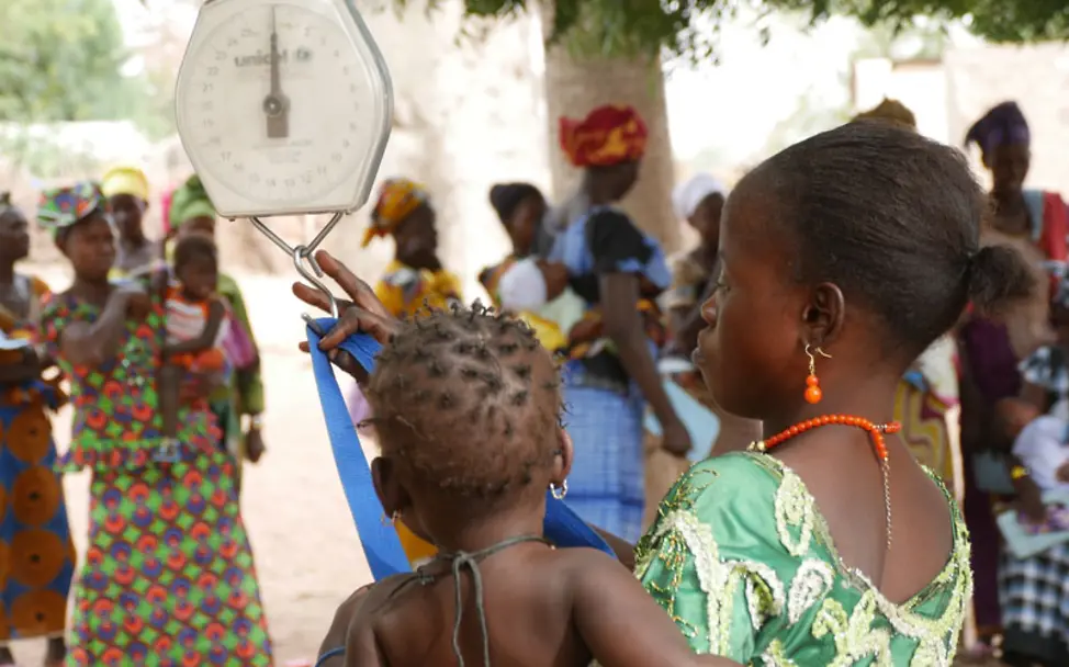 Ein Baby wird an einer Hängewaage gewogen| © UNICEF/Karina Hövener Gambia Reise: Ein Baby wird an einer Hängewaage gewogen