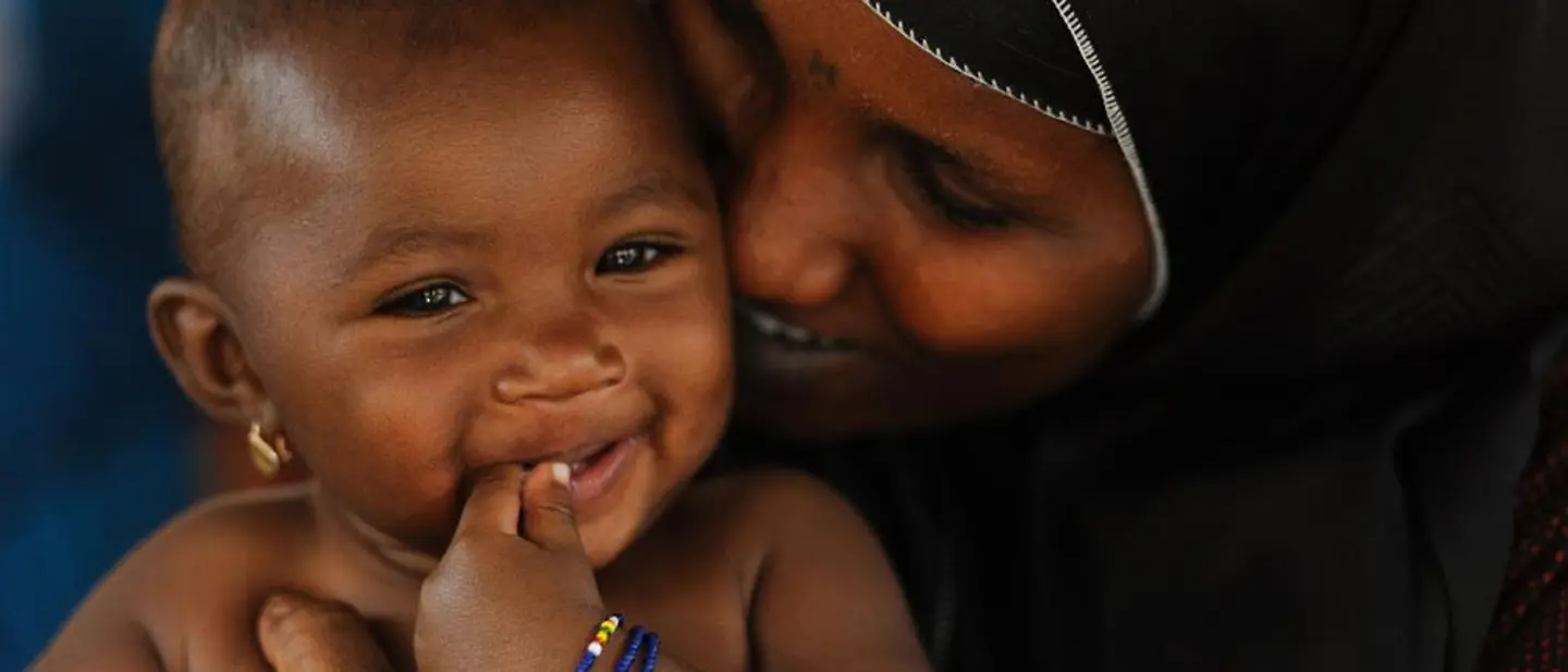 Eine Mutter umarmt lächelnd ihr lachendes Baby von hinten.