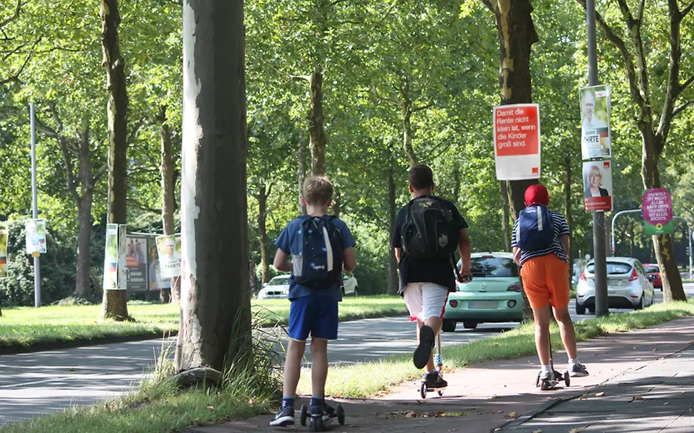Bundestagswahl 2017: Kinder fahren mit Rollern an Wahlplakaten vorbei