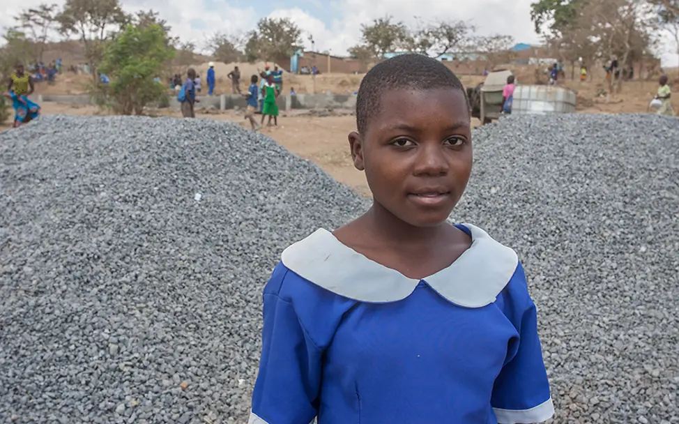 Aness freut sich über die Fortschritte beim Schulbau. | © UNICEF Malawi/2018/Amos Gumulira Malawi: Aness steht vor der Schulbaustelle.