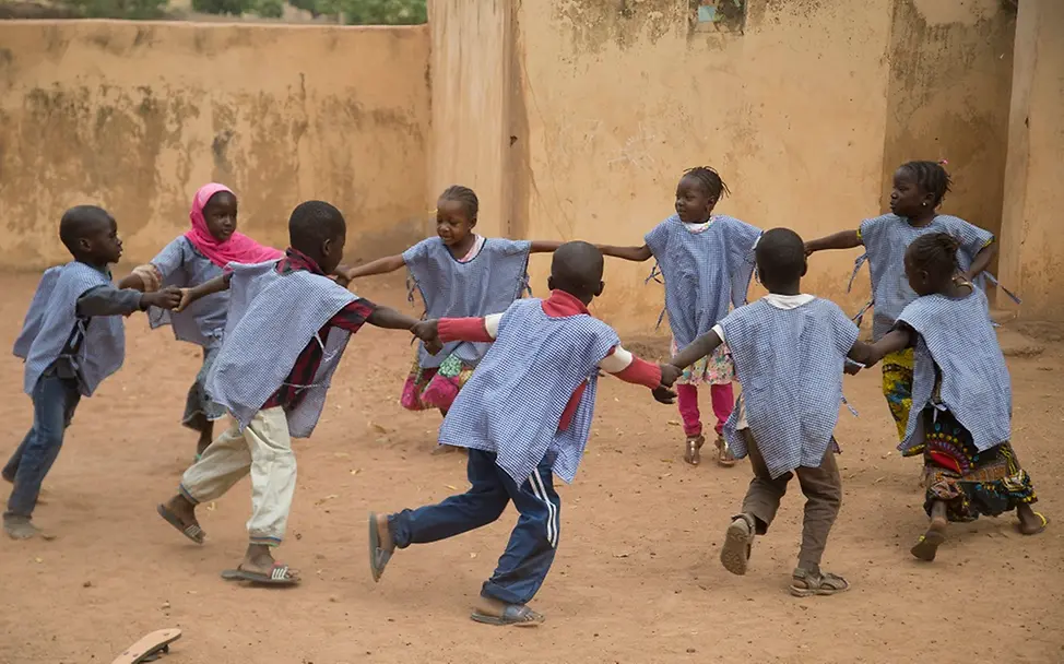 Kinder spielen in einem Zentrum für frühkindliche Entwicklung im Dorf Baraouéli/Mali. | © UNICEF/UN0160954/Keïta Mali: Kinder drehen sich händehaltend im Kreis vor einem Lehmhaus