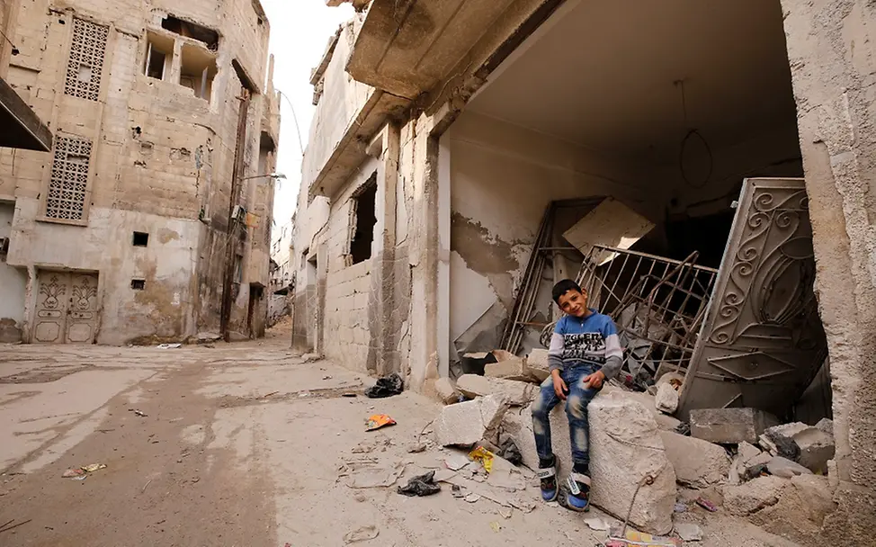 Ein Junge sitzt vor den Ruinen eines Wohnhauses.