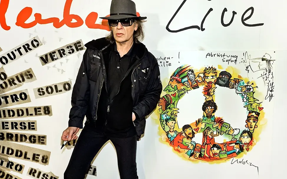 Udo Lindenberg vor einer Wand mit selbst designetem Peace-Zeichen.