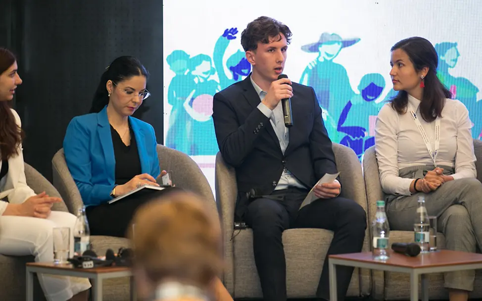 Bastian möchte wie viele andere Jugendliche gehört werden. | © UNICEF Rumänien Bukarest: Bastian mit drei weiteren Personen auf dem Podium der Opening Session.