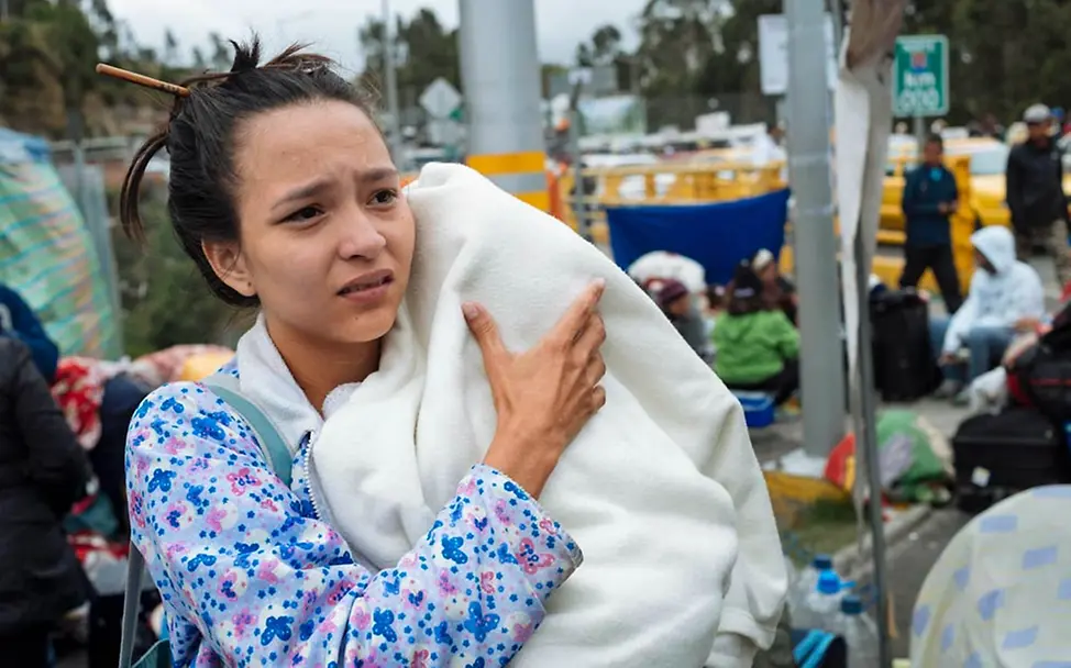 Angespannt wartet eine junge Mutter mit ihrem Baby an der Grenze. | © UNICEF/Arcos Eine junge Mutter trägt schützend ihr Baby auf dem Arm.