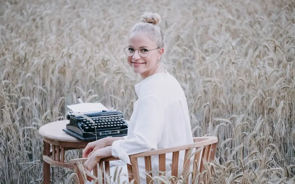 Die Autorin und Dichterin Julia Engelmann setzt sich für UNICEF und Kinder weltweit ein. | © Marta Urbanelis Dichterin und Autorin Julia Engelmann sitzt an einer Schreibmaschine im Kornfeld.