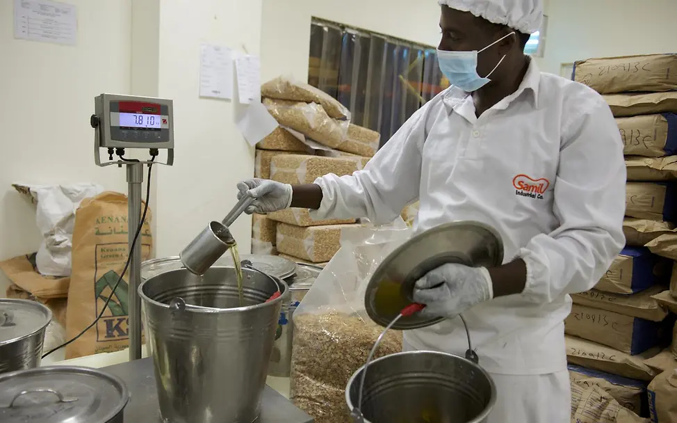 Erdnusspaste-Fabrik im Sudan: Ein Mitarbeiter fügt den Erdnüssen Öl hinzu | © UNICEF/Noorani Erdnusspaste-Fabrik im Sudan: Ein Mitarbeiter fügt den Erdnüssen Öl hinzu