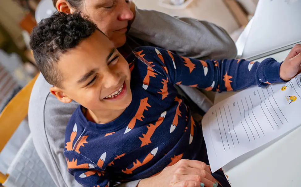 Der Junge hat Spaß, die Mutter wirkt erschöpft. | © UNICEF/McIlwaine Kinderschutz: Mutter hilft ihrem Sohn bei Schulaufgaben.