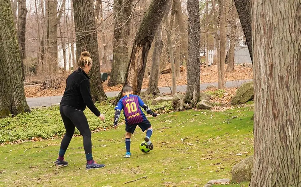 Luka (8) spielt mit seiner Mutter Sophia Fußball in einem Waldstück. | © UNICEF/McIlwaine USA: Luka (8) spielt mit seiner Mutter Sophia Fußball in einem Waldstück.
