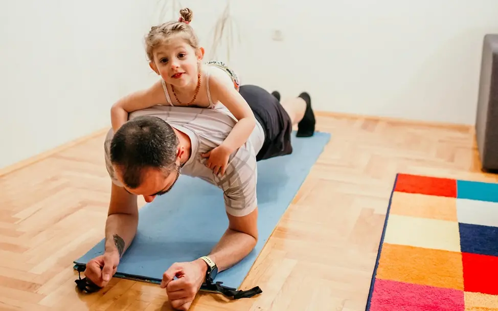 Der Vater wird beim Sport machen fleißig unterstützt. | © UNICEF/Isanovic Bosnien und Herzegowina: Lana klettert auf Rücken des Vaters.