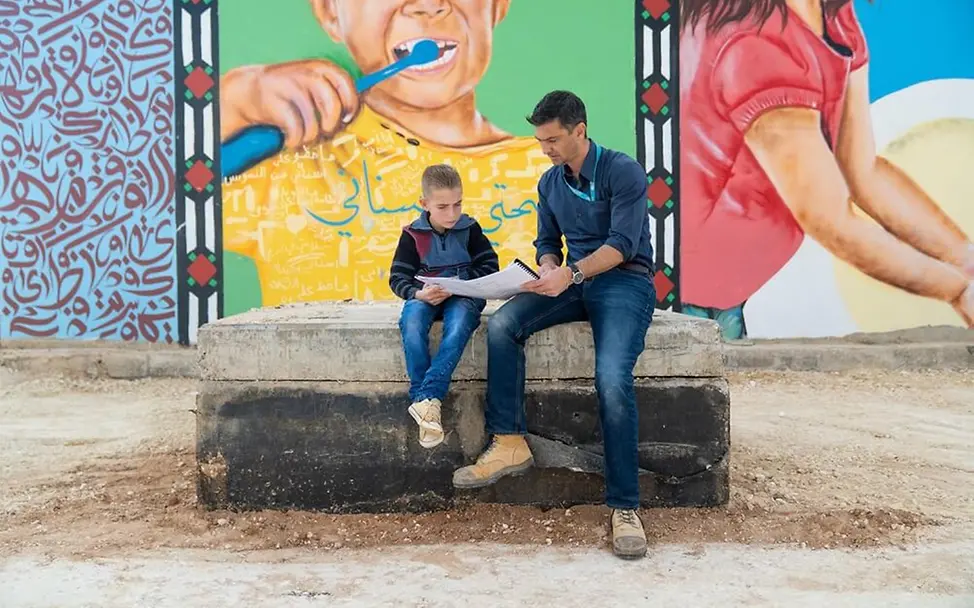 Ben Smith zeigt Ahmad, wie die Wasserversorgung funktioniert. | © UNICEF/Herwig Flüchtlingscamp Zaatari: Ein UNICEF-Mitarbeiter mit Ahmad.