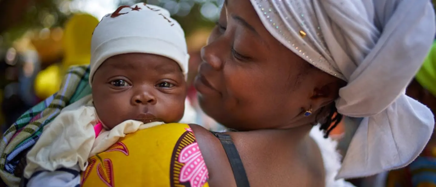 Vorsorgeuntersuchung in Gambia: Eine Mutter lässt ihr Baby impfen und messen. | © UNICEF/Noorani Eine Mutter hält ihr Baby auf dem Arm.