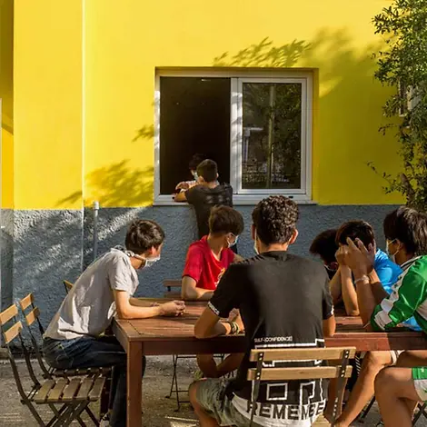 Mehrere geflüchtete Jugendliche sitzen zusammen im Hof des Kinderzentrums an einem Tisch.