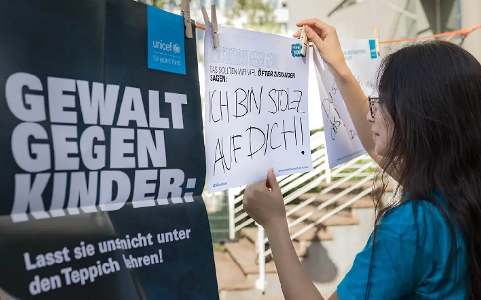 UNICEF-Aktion: Ein Mädchen hängt ein Plakat zum Thema Gewalt gegen Kinder auf. | © UNICEF/Herbach UNICEF-Aktion: Ein Mädchen hängt ein Plakat zum Thema Gewalt gegen Kinder auf.