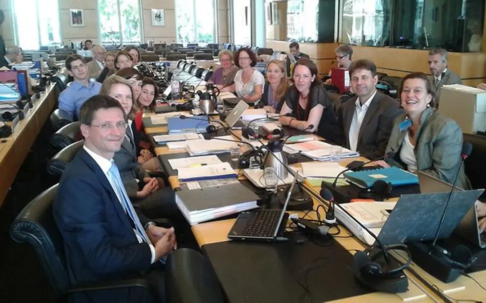 Abgeordnete sitzen sich an einem langen Tisch gegenüber.