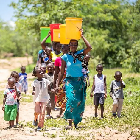 Frauen tragen bunte Eimer auf ihren Köpfen.