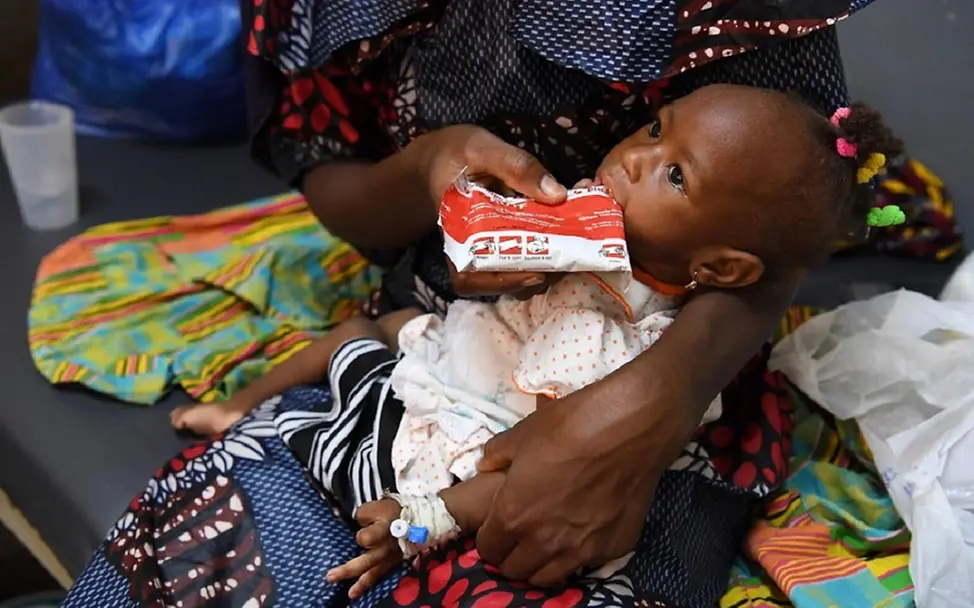 Jede Minute ein weiteres Kind schwer mangelernährt | © UNICEF/Dejongh Burkina Faso: Kind im Schoß der Mutter bekommt therapeutische Nahrung