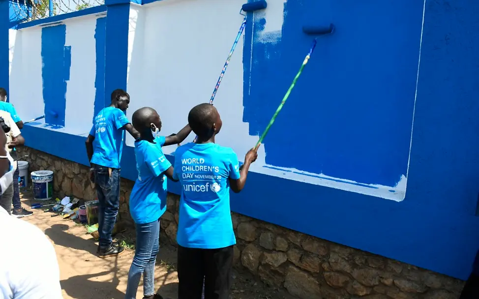 Südsudan: Kinderreporter streichen einen Zaun blau.