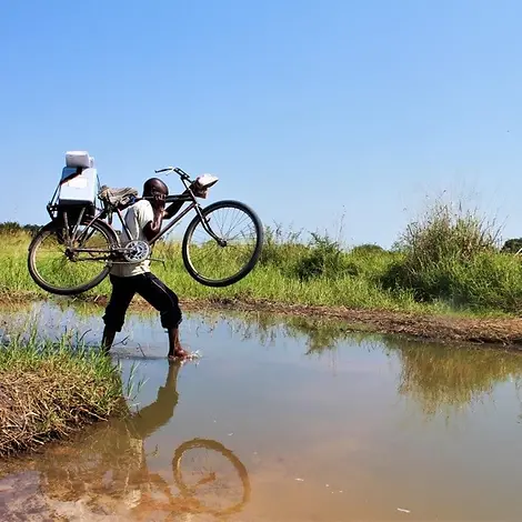 Impfstoffe für den Südosten der Demokratischen Republik Kongo. | © UNICEF/Wingi Demokratische Republik Kongo: Ein Helfer trägt Hilfsgüter auf einem Fahrrad über einen Fluss.