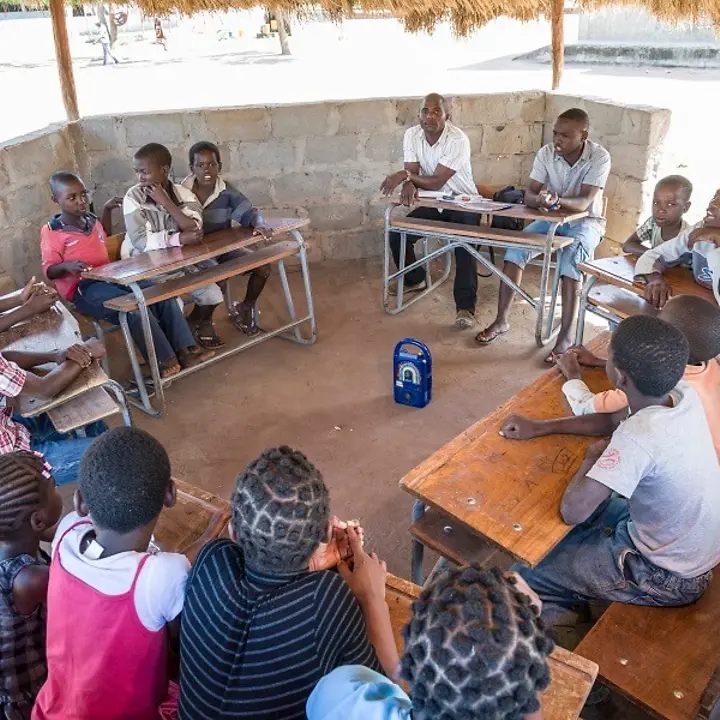 Kinder sitzen an Schultischen um das Radio herum