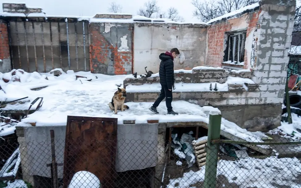 Ein Junge und sein Hund spazieren im Schnee vor dem zerstörten Haus seiner Familie. | © UNICEF/Filippov Ukraine-Krieg: Ein Junge und sein Hund spazieren im Schnee vor dem zerstörten Haus seiner Familie