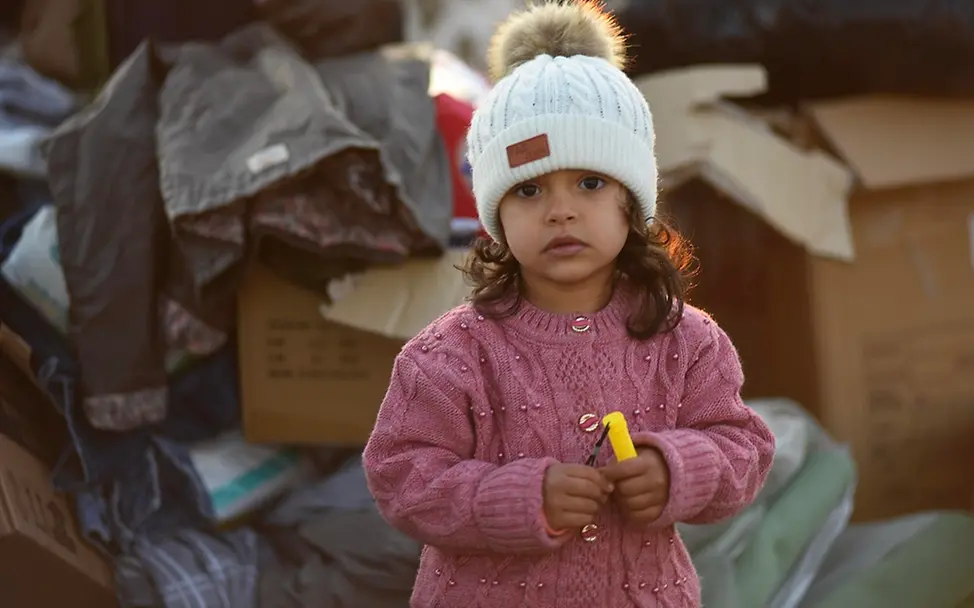 Erdbeben in der Türkei und Syrien: Hunderttausende Kinder leben unter verzweifelten Bedingungen I UNICEF/Ölçer Ukraine: Ein Mädchen steht vor Boxen mit Hilfsgütern und schaut in die Kamera.