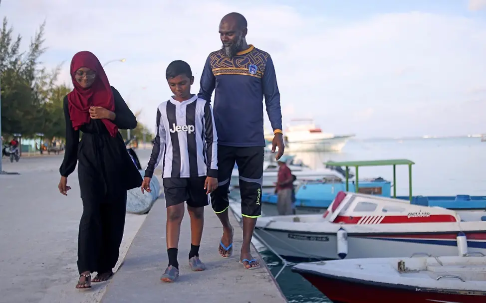 Ein Spaziergang durch den Hafen. | © UNICEF/Faheem Malediven: Fathimath spaziert mit ihrem Vater und ihrem Bruder am Hafen entlang, neben ein paar kleinen Booten.