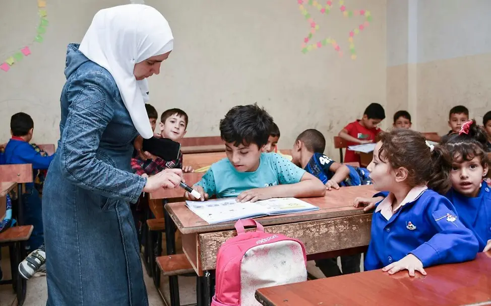 Syrien: Ahmad sitzt im Matheunterricht und schaut sich mit seiner Lehrerin sein Aufgabenheft an.