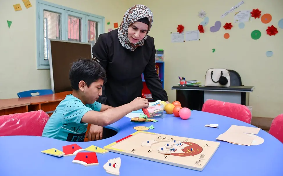 Syrien: Ahmad und seine Lehrerin sitzen vor einem Lernspiel.