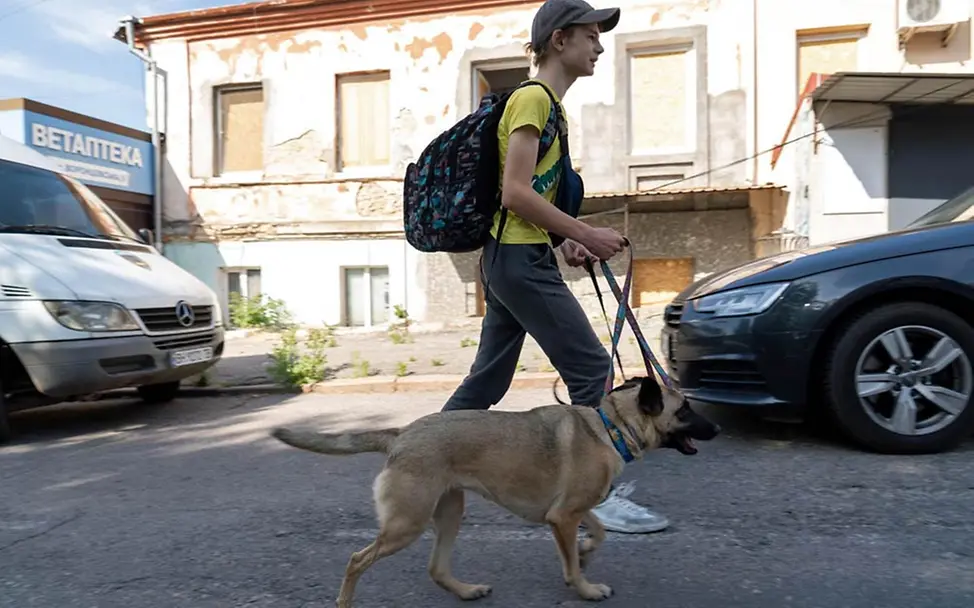 Ein Junge geht nach der Evakuierung mit seinem Hund durch die Straßen von Cherson. | © UNICEF/UN0853468/Filippov Zerstörter Kachowka-Staudamm: Tausende Kinder müssen evakuiert werden.