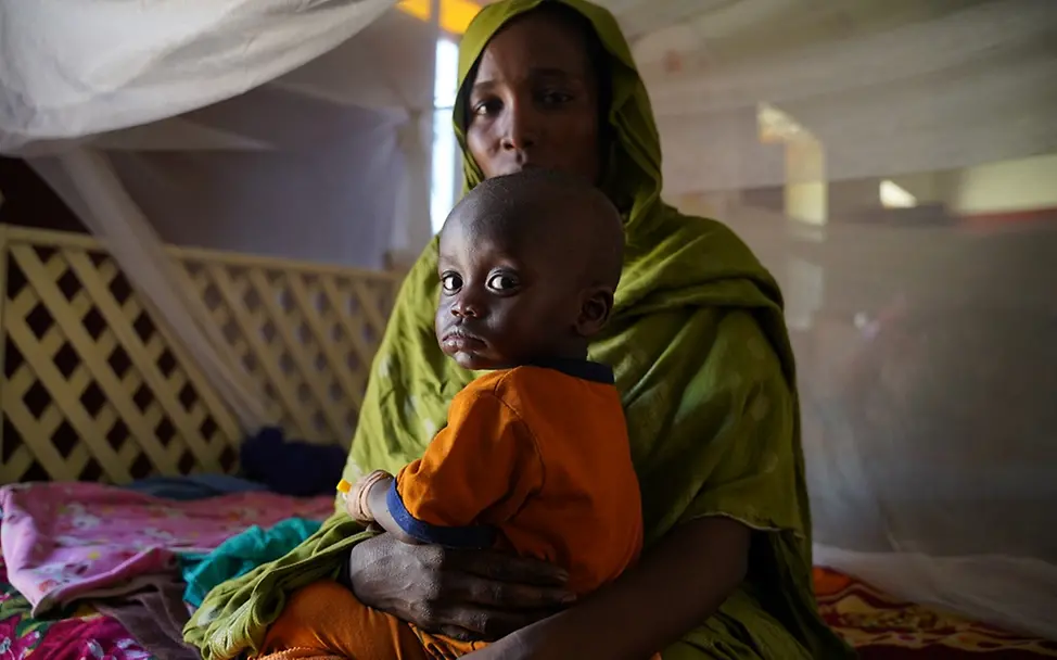 Sudan: Ein Kind sitzt auf dem Schoß seiner Mutter und beide schauen in die Kamera