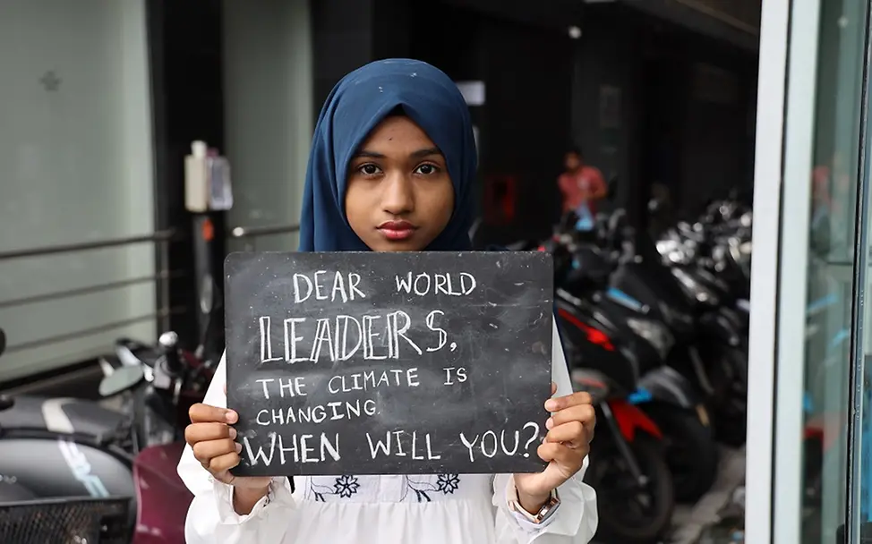 Malediven: Ein Mädchen hält eine Tafel vor ihren Körper Richtung Kamera.