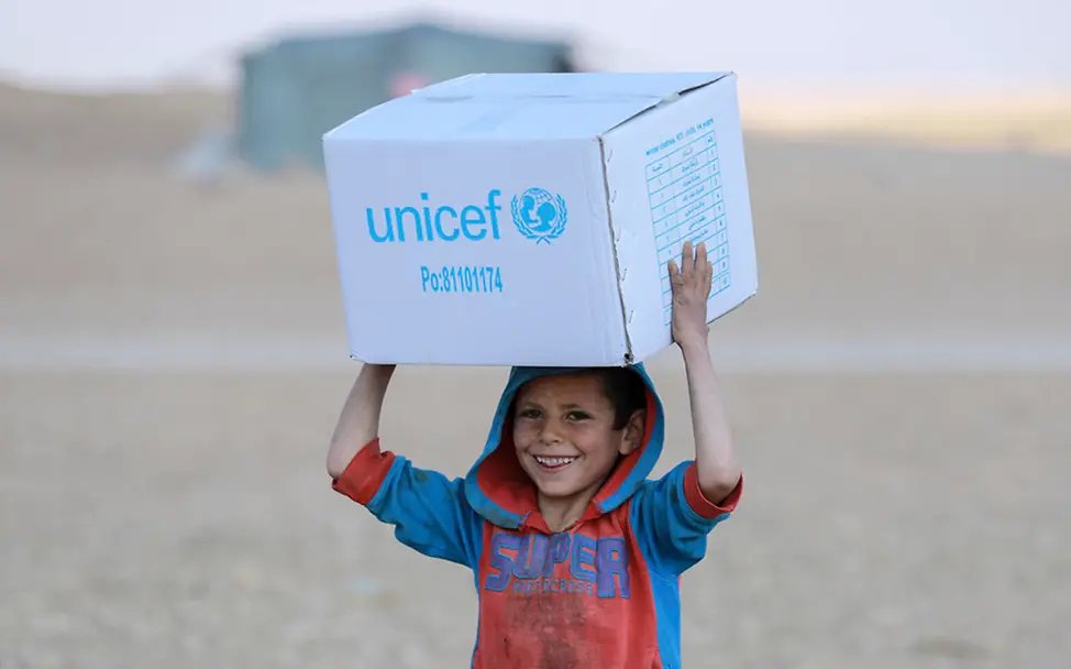 Syrien: Ein Junge trägt einen Karton mit Hilfsgütern von UNICEF | © UNICEF/Souleiman Originelle Geschenkideen für guten Zweck: Junge trägt einen Karton mit Hilfsgütern von UNICEF in Syrien