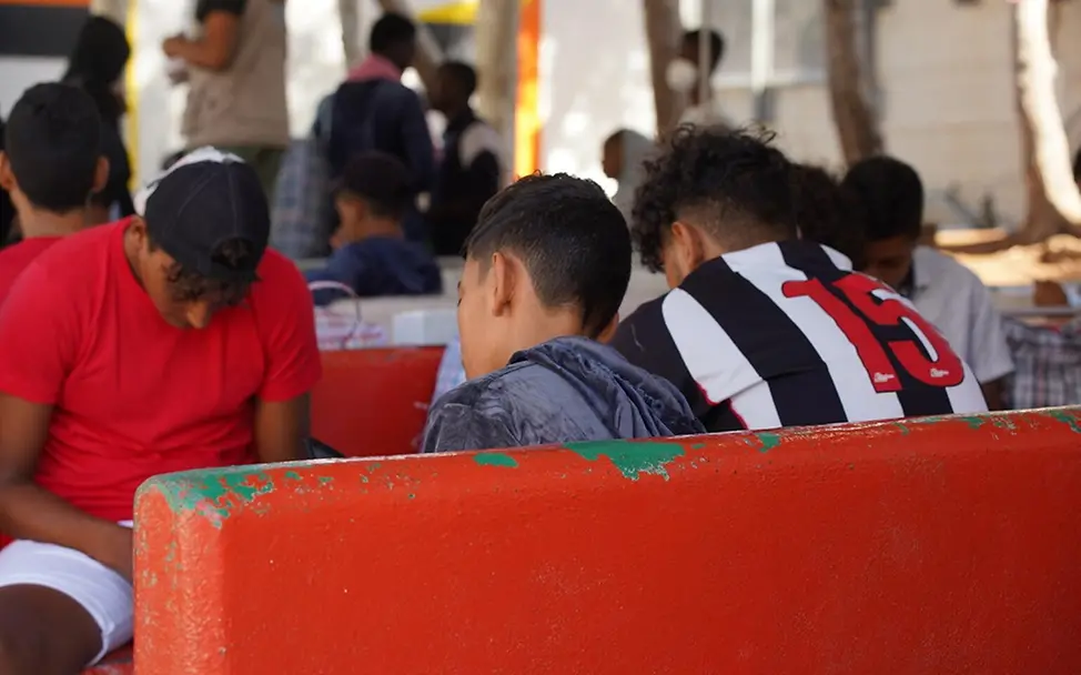 Kinder und Jugendliche in einer Aufnahmeeinrichtung | UNICEF/Corti Drei Jugendliche sitzen auf Bänken in einer Aufnahmeeinrichtung