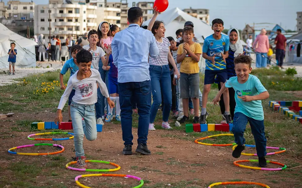 Geflüchtete Kinder in Syrien springen in einem UNICEF-Kinderzentrum über bunte Reifen | © UNICEF/Issa UNICEF/UNI419763/Issa
