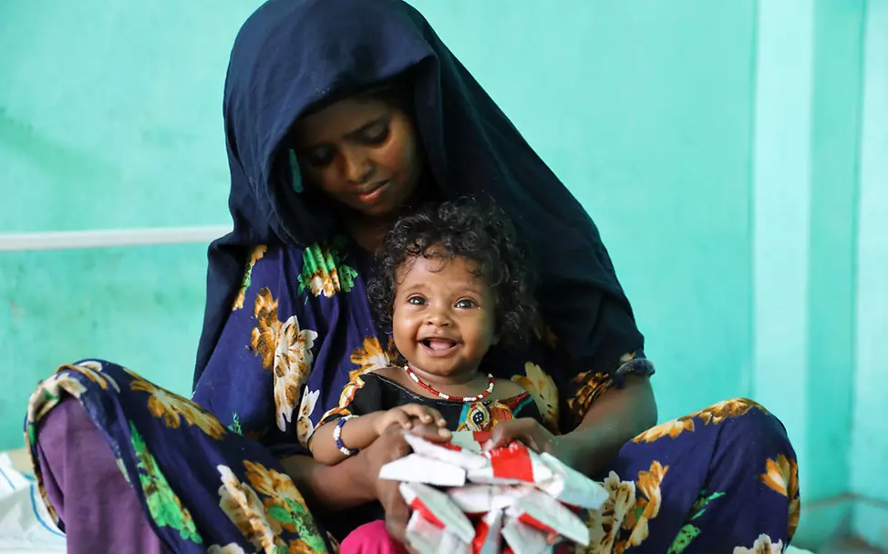 Eine Mutter in Äthiopien mit ihrem Baby und vielen Päckchen Erdnusspaste | © UNICEF/Assefa Eine Mutter in Äthiopien hat für ihr mangelernährtes Baby Erdnusspaste bekommen.