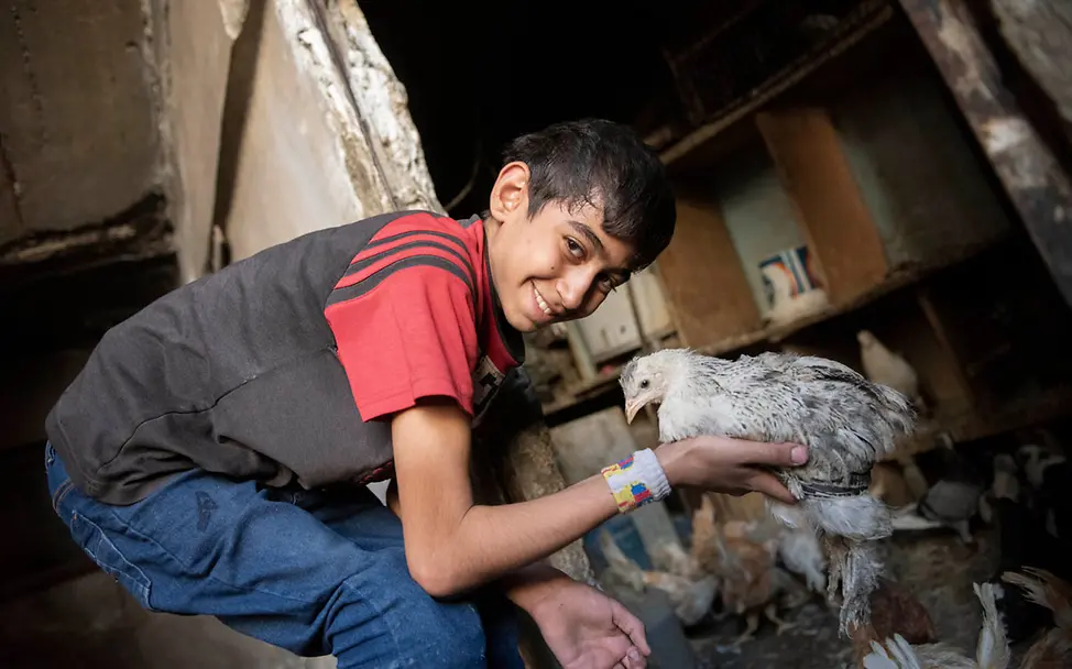 Ein Junge in Syrien spielt lächelnd mit einem Huhn. | © UNICEF/Belal Ein Junge in Syrien spielt lächelnd mit einem Huhn.