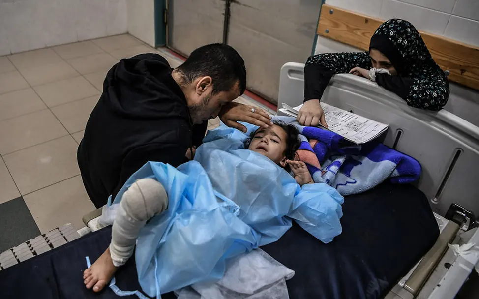 Kinder in Gaza: Ghazal (4) wurde am Fuß verletzt und braucht dringend medizinische Versorgung | © UNICEF/Zaqout Die vierjährige Ghazal liegt weinend in einem Krankenhausbett. Ihr Vater sitzt neben ihr und streichelt ihre Stirn.