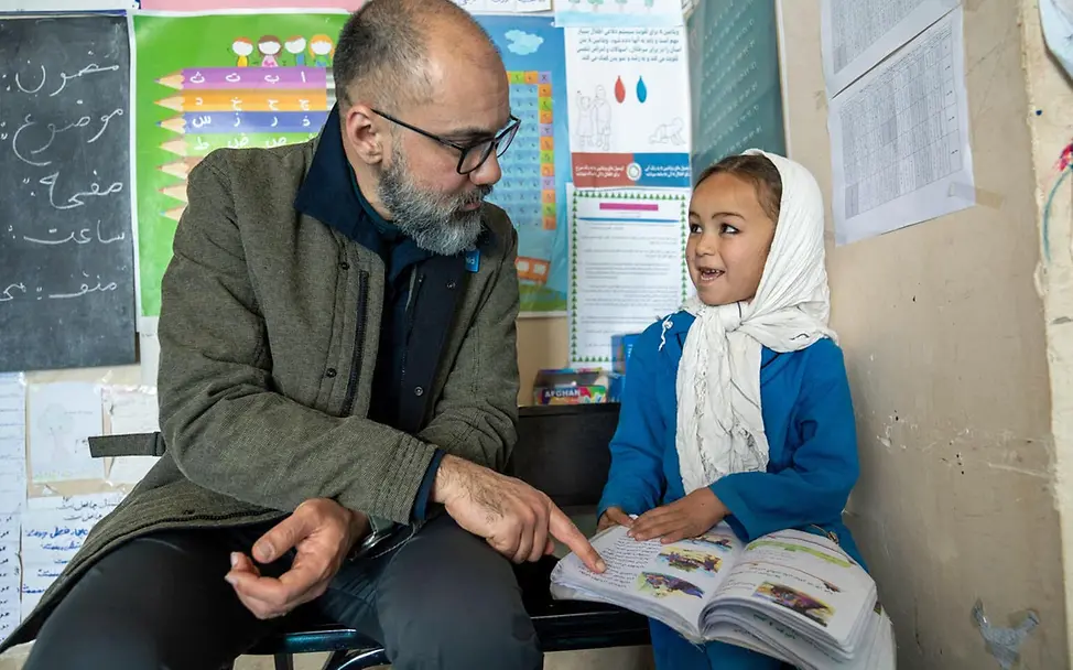 Eine Schülerin in Afghanistan im Gespräch mit einem UNICEF-Helfer | © UNICEF/Karimi Spenden Afghanistan: UNICEF-Bildungsprojekte: Eine Schülerin zeigt einem UNICEF-Mitarbeiter ihr Schulbuch