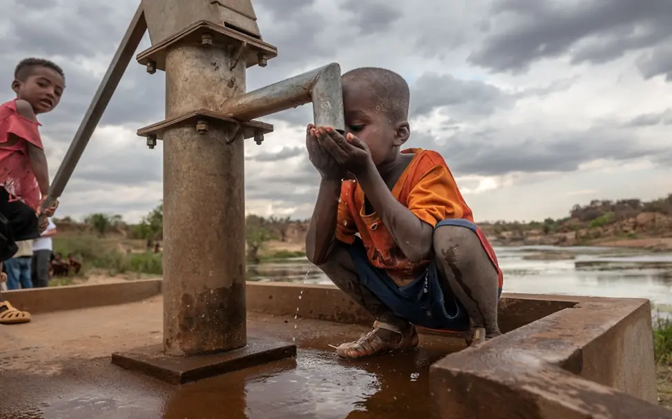 Madagaskar | © UNICEF/UNI658473/Andrianantenaina Zwei Jungen helfen sich gegenseitig, während der eine Wasser pumpt und der andere trinkt.