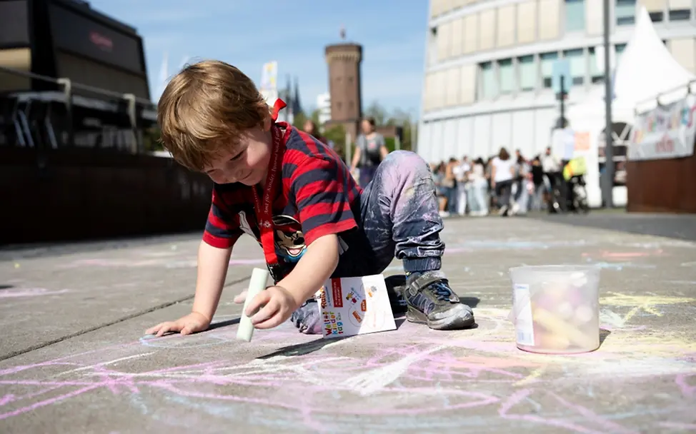 Weltkindertag: Ein Kind malt mit Straßenkreide auf der Straße.