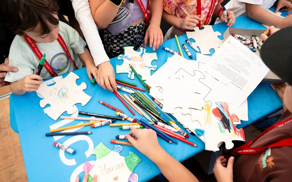 Weltkindertag: Kinder malen mit Buntstiften auf großformatige Puzzle-Teile aus Pappe.