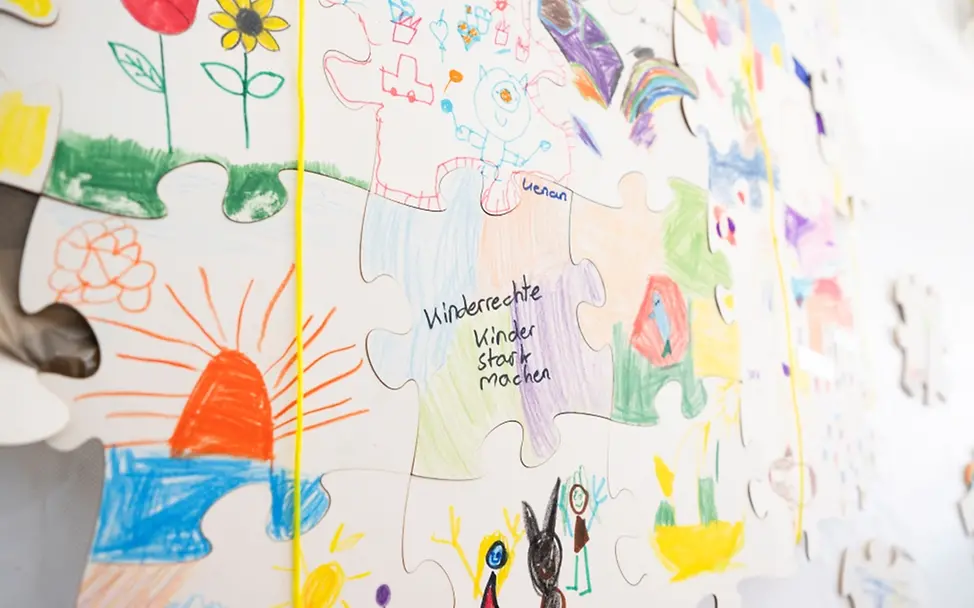 Weltkindertag: Großaufnahme von den von Kindern bemalten Puzzle-Teilen aneinander gefügt an der Wand.