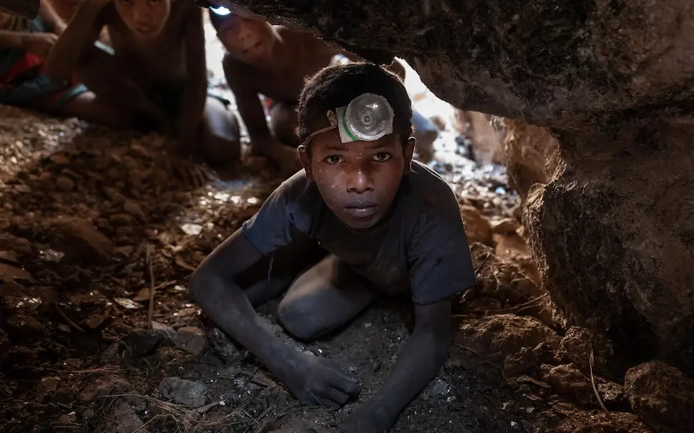 Sambilahatsa arbeitet tief unter der Erde in einer Glimmermine. | © UNICEF/Andrianantenaina Was kann man gegen Kinderarbeit tun: Ein Junge hockt mit einer Stirnlampe in einer Glimmermine in Madagaskar.