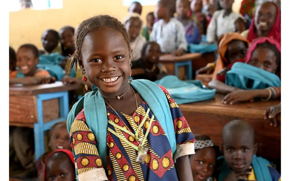 Chad: Mädchen sitzt mit einem UNICEF-Rucksack auf dem Rücken in einem Klassenzimmer.