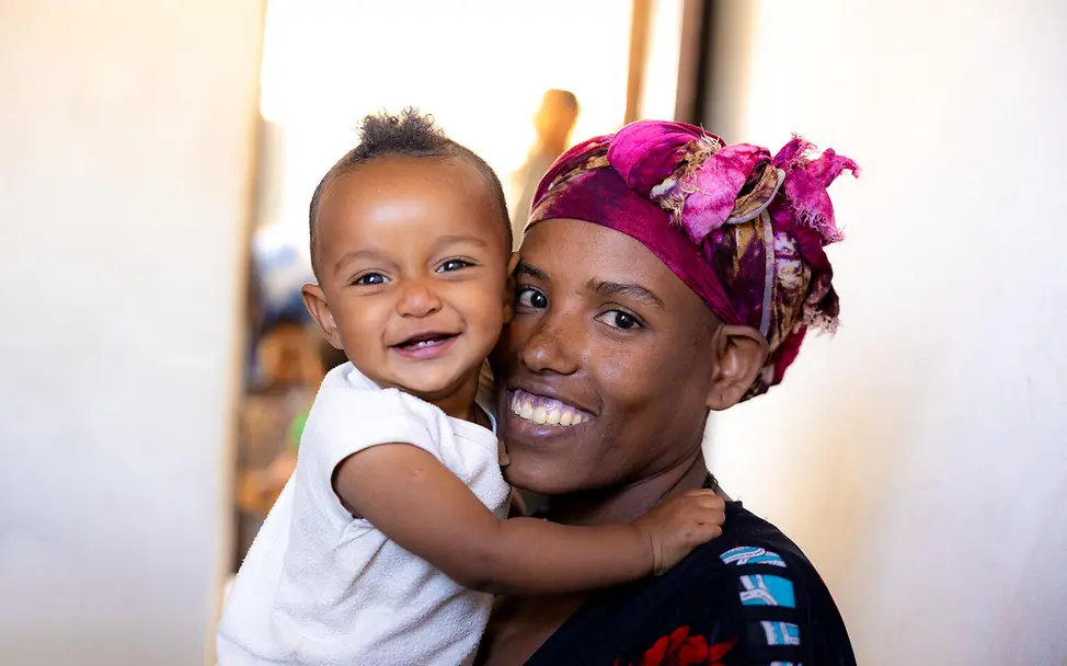 Impfungen Baby: Ein lächelndes gesundes Baby auf dem Arm seiner Mutter in Äthiopien. 