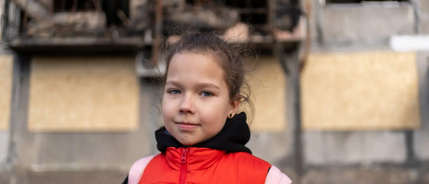 Ein Mädchen in der Ostukraine steht vor einem stark beschädigten Wohnhaus | © UNICEF/Filippov Ukraine Spenden: Angriffe bringen Kinder wie dieses Mädchen in Gefahr