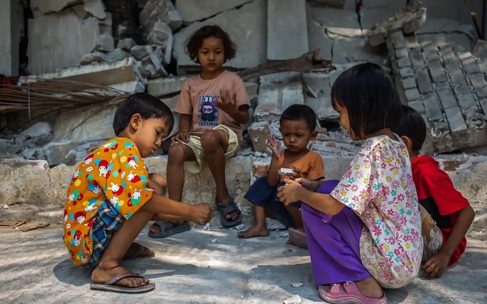 Hilfe für Myanmar: Poe Kyal Sin Lin (6) und andere Kinder sitzen vor einem eingestürzten Gebäude.