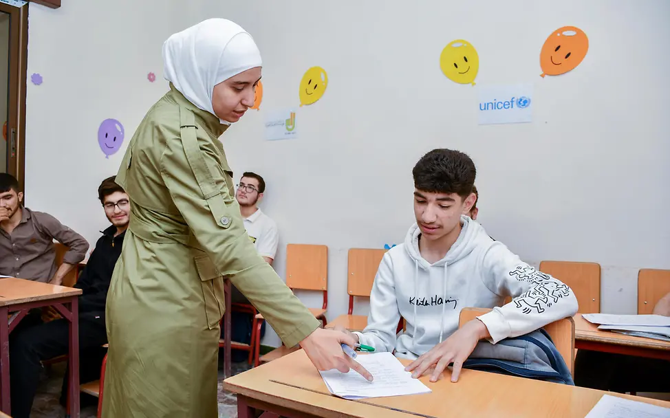 Der 17-jährige Bilal sitzt in der Schule und seine Lehrerin erklärt ihm etwas zu der Aufgabe auf seinem Tisch. 