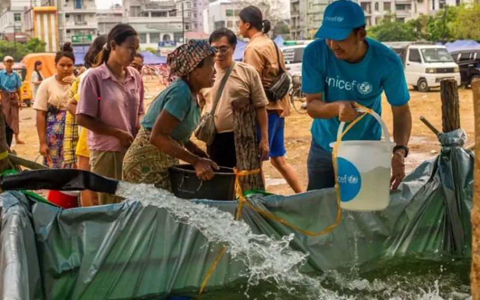 Myanmar Erdbeben spenden: Ein UNICEF-Helfer schöpft mit einem Eimer Wasser. 